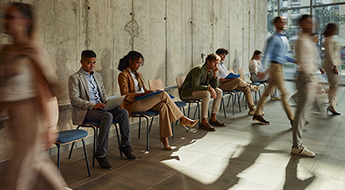 people waiting for interview; some are working on laptops and some look depressed