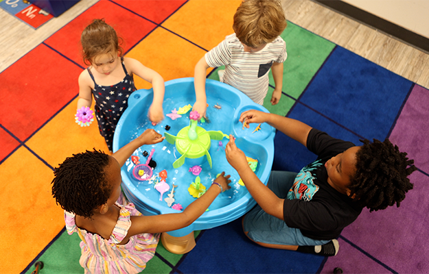 four kids playing around a water bassin in a classroom
