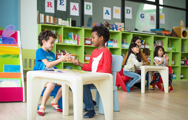 two preschoolers play at a table in a classroom