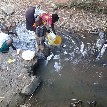 woman fetching water from reservoir with two young children nearby